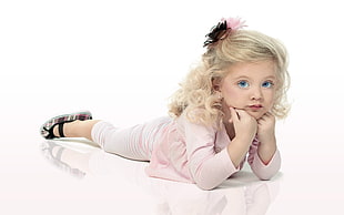 girl wearing pink long-sleeve shirt and white pants laying on floor