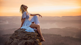 woman wearing white dress sitting on rock formation during golden hour