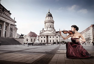 photo of woman in brown dress playing violin near white palace
