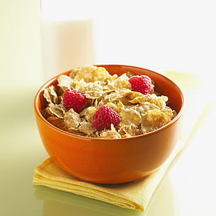cereal flakes with raspberry on orange ceramic bowl
