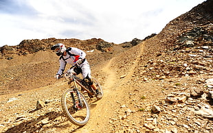 man wearing white racing suit riding on brown full-suspension mountain bike