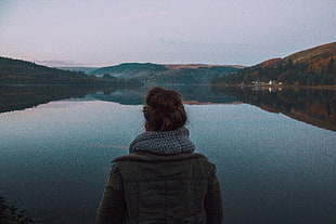person wearing gray jacket in front of  body of water and mountain