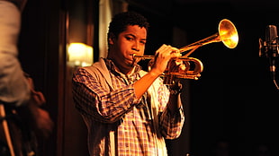 man in brown plaid dress shirt playing brass trumpet