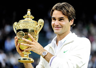 man in white Nike jacket smiling and holding gold-colored trophy