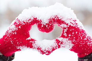 person's hand wearing red gloves forming heart shape covered in snow at daytime