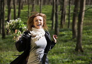 woman in black leather jacket holding flowers running near brown trees