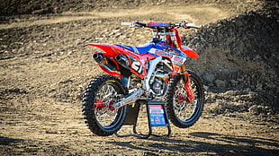red, orange, and blue dirt bike on gray metal paddock stand