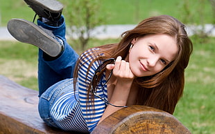 woman in striped shirt lying on wooden stump log bench outdoors during daytime