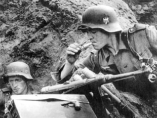 grayscale photo of men soldiers near rock lighting cigarette