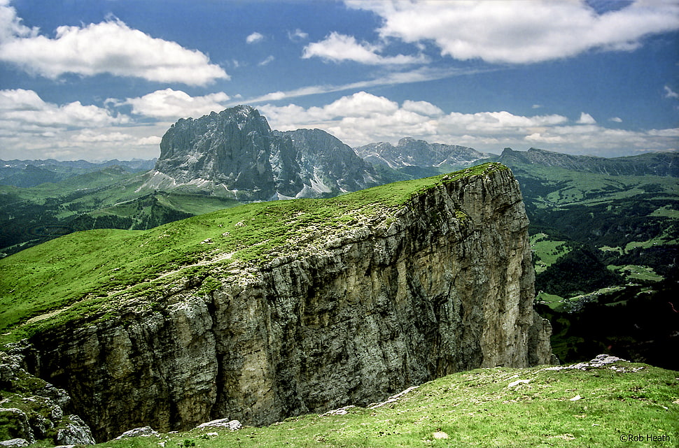 grassy stone cliffs across cloudy mountains during daytime HD wallpaper