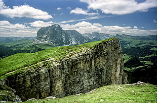 grassy stone cliffs across cloudy mountains during daytime