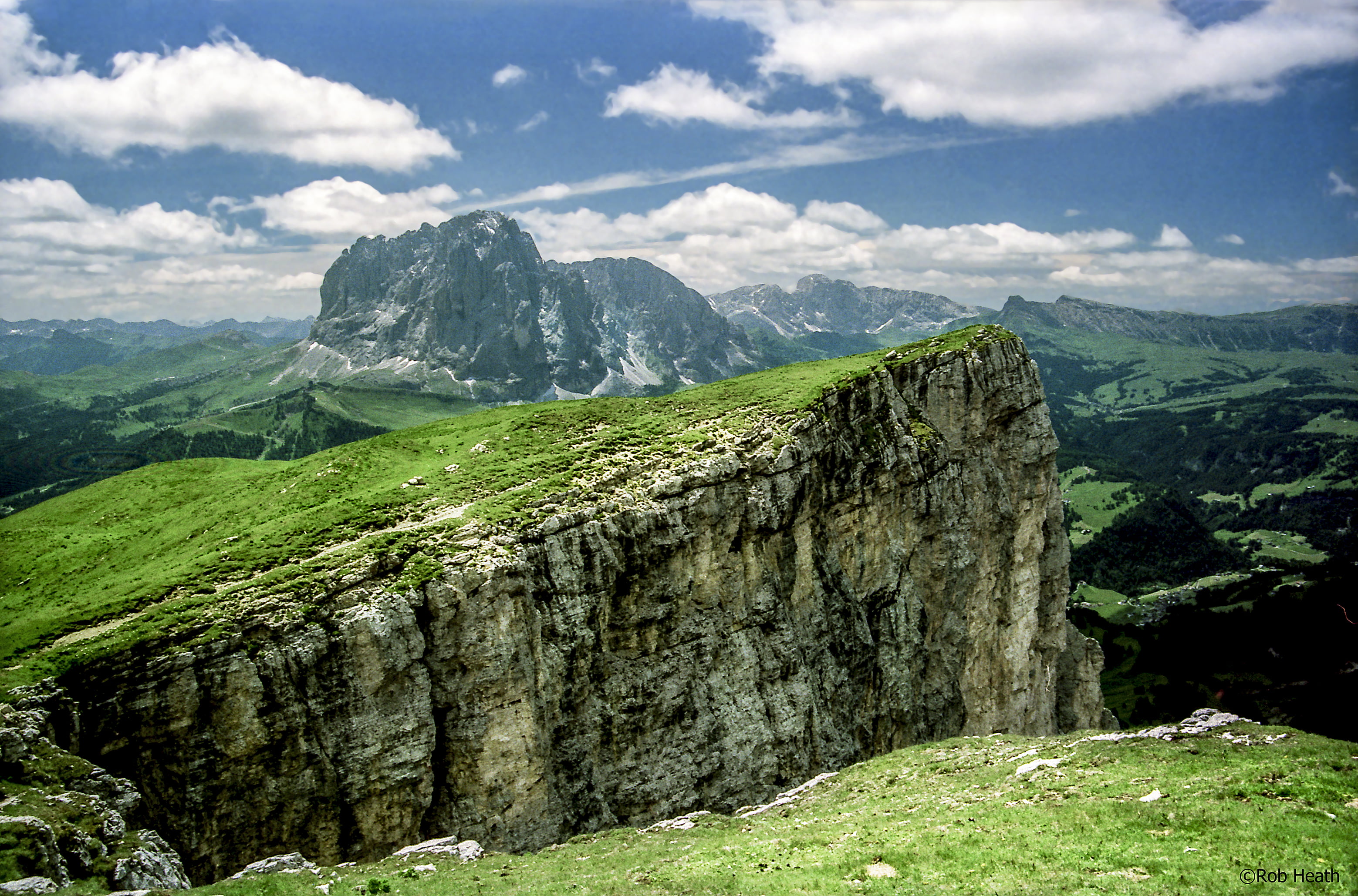 grassy stone cliffs across cloudy mountains during daytime