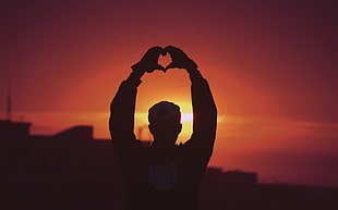 silhouette of man making heart hand sign