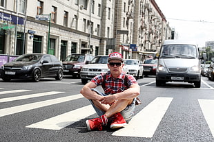man in red and black plaid button-up t-shirt with gray shorts and pair of red-and-white high-top sneakers on road near gray van during daytime HD wallpaper