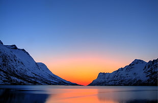 body of water surrounded by snow covered mountains during sunset