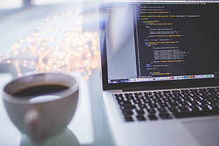 white coffee cup beside silver MacBook