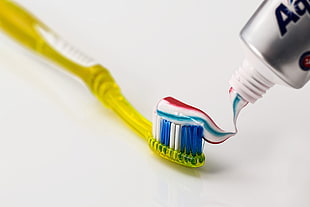 yellow toothbrush with red-white-and-blue toothpaste on top
