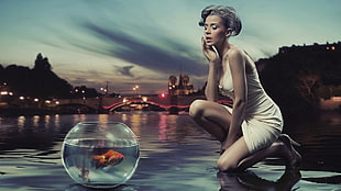 woman in white body con dress looking at glass bowl with gold fish