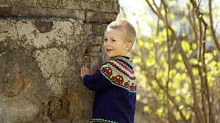 toddler's wearing blue and green sweater beside concrete wall