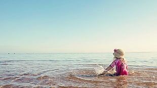 girl in pink shirt and brown sun hat on seashore