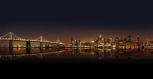 lighted bridge across body of water towards inline high-rise buildings mirrored on calm body of water