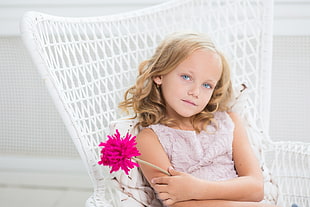 girl holding pink flower sitting on white armchair
