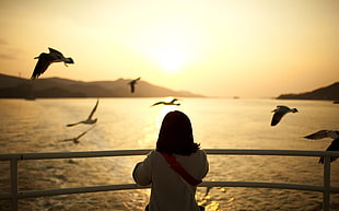 photo of woman standing beside body of water during sunset