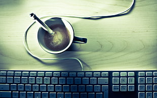 black ceramic mug filled with coffee near corded computer keyboard