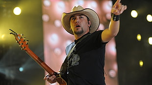 man wearing cowboy hat holding guitar pointing