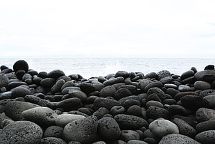 pile of rocks beside beach under clear white sky