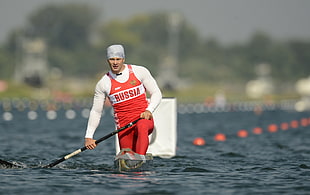 man wearing red and white long-sleeved Russia print wet suit on water during daytime
