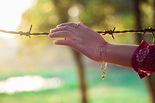 person's left hand wearing gold bracelet while holding brown steel barbwire