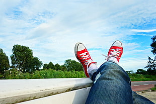 person wearing red low top sneakers under cirrus clouds