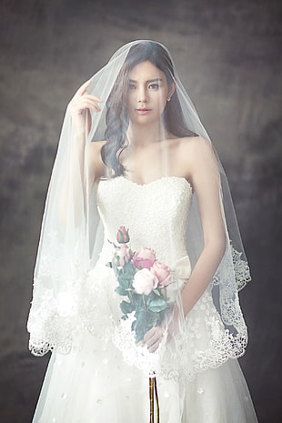 woman in white bridal gown with veil holding bouquet of flower