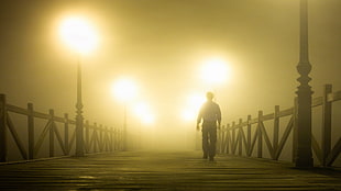 man in black pants walking on wooden bridge with light turned on, niebla