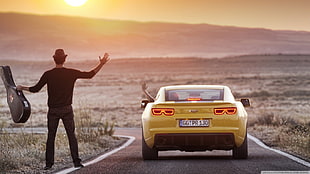 person standing waving on person driving yellow car