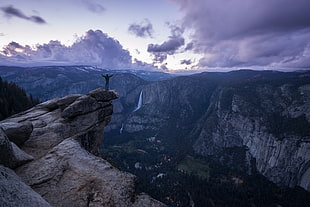 man raising hands on cliff