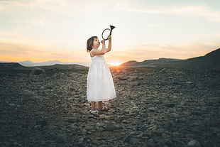 girl in white dress playing wind instrument standing on stone field
