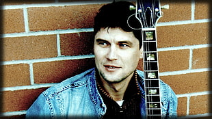 man in blue denim jacket holding black guitar