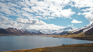 large body of water near icy mountains under cloudy sky during daytime