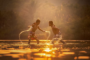 Two Man Fighting in body of water during  sunset HD wallpaper