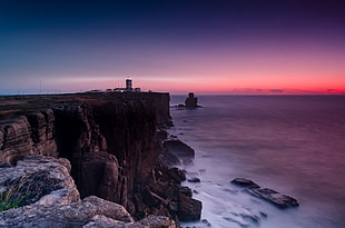 landscape photography of cliff beside ocean under sunset