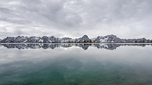 Reflective snowy mountains under cloudy sky