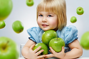 girl in blue dress holding green apples