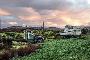 green rusted utility truck beside white boat on green grass field under white skies