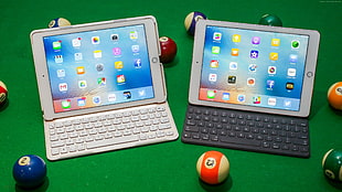 two silver iPad turned-on on black and white keyboards near billiard balls