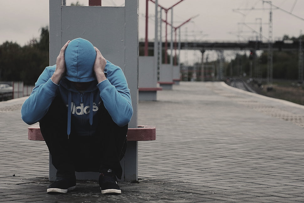 man in blue Adidas pull-over hoodie and black pants sitting on gray concrete floor HD wallpaper