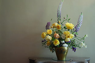 yellow petaled flower with gold-colored vase on brown wooden side table