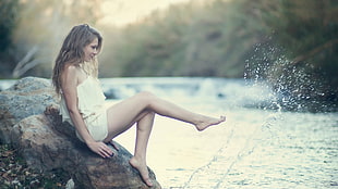 time lapse photograph of woman sitting on rock with water splash