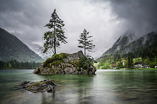 rock formation on body of water near mountains under gray clouds during daytime HD wallpaper